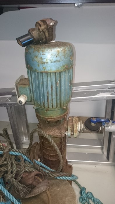 En gammal, rostig vattenpump med blåfärgad topp och diverse kopplingar, omgiven av rep.