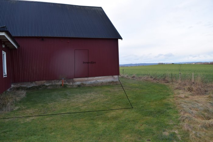 Markering av grunden för två sovrum bredvid en röd byggnad med landskap i bakgrunden.