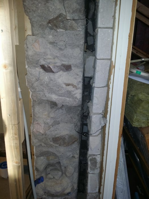 Delvis upplyst murad vägg med synliga gamla och nya lager av sten och murbruk i ett renoveringsprojekt.