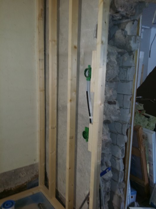 Oisolerat väggramverk av träreglar framför gammal murad stenvägg, med synlig elinstallation, under byggnadsprocess.