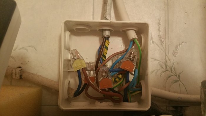 Öppen elektrisk anslutningsdosa med ordnade kablar och säkerhetskåpor på vägg.
