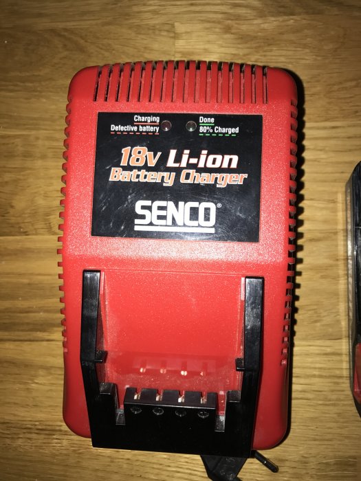 Röd Senco 18V Li-ion batteriladdare på ett träbord, i nyskick, utan batterier monterade.