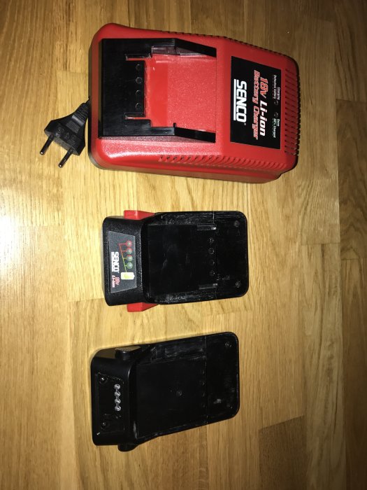 En Senco 18V laddare och två batterier på ett trägolv.