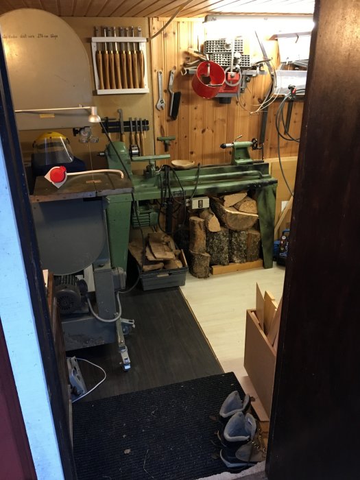 Utsikt från dörren till en välorganiserad snickarbod med svarv, verktyg upphängda på väggen och vedträn.