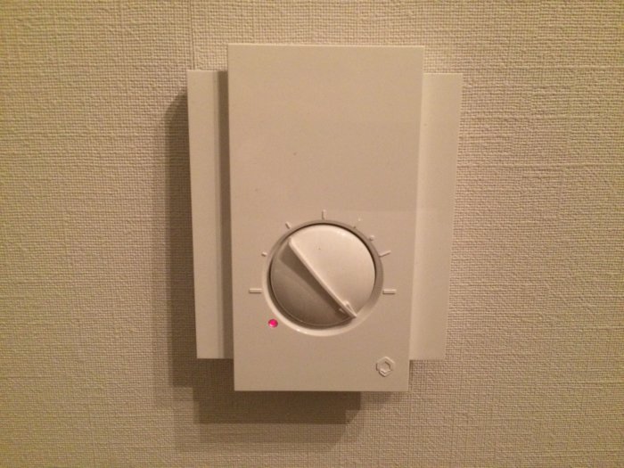 Rumsgivare på vägg med inställningsvred och röd lysande indikatorlampa.