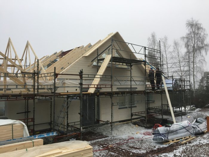 Monteringsarbete på ett hus under konstruktion med trästomme och byggnadsställningar.