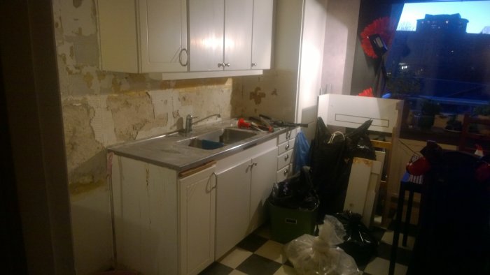 Kök under renovering med ommålade luckor och vägg utan kakel, renoveringsbråte syns.