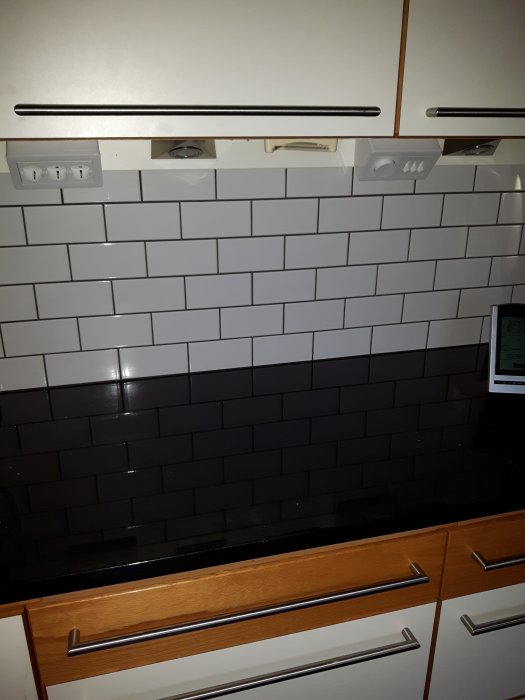 Vit och svart metrokakel i kök med förskjutna skarvar ovanför arbetsyta och trädetaljer.