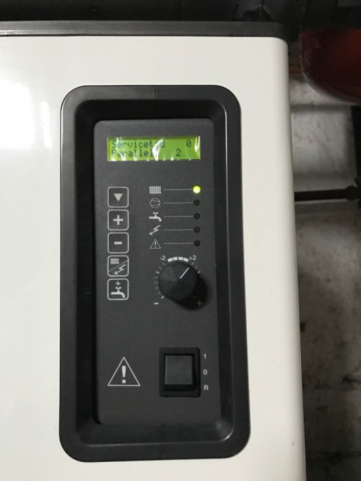 Värmepumpens kontrollpanel med display som visar serviceinställningar och en ratt inställd på +2.