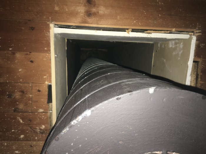 Svart rör genom en öppning i taket, tidigare del av installation för braskamin i källare.