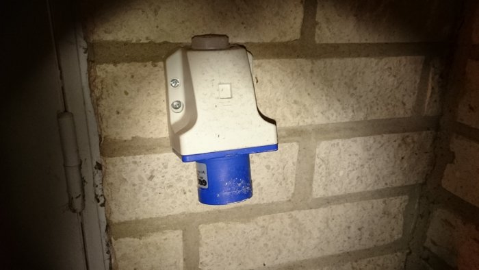 Blått uttag på grå vägg för utomhuskoppling av elverk.
