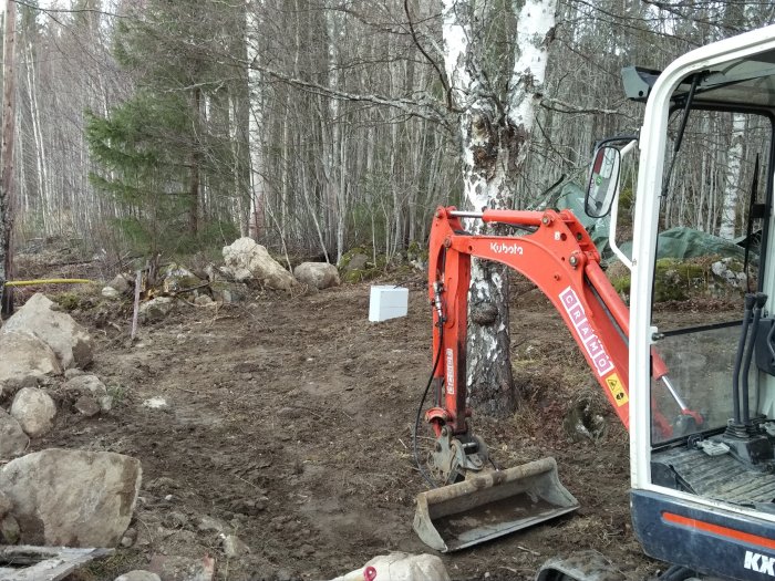 Nytt mätarskåp placerat utomhus bredvid en grävmaskin i ett skogsmarkområde under byggarbete.