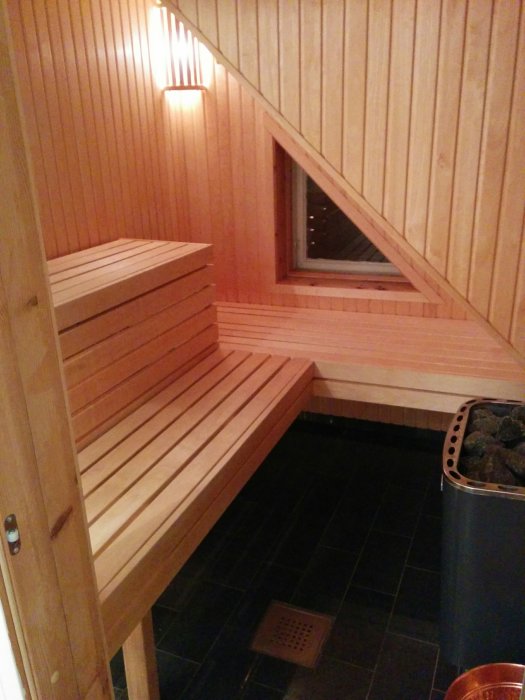 Inredning av bastu med träbänkar och snedtak, vedugn synlig längst in.