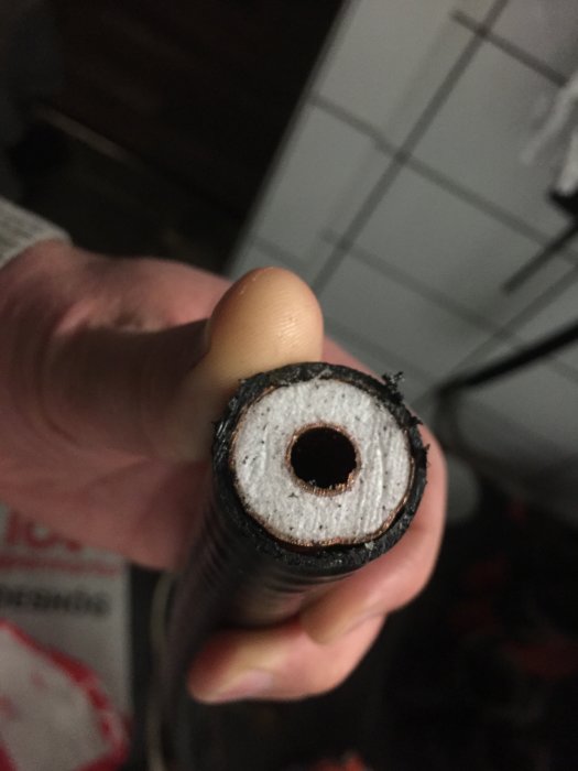Hand som håller en tvärsnitt av isolerad rörledning med kopparrör, isoleringsmaterial och yttre plastskaft.