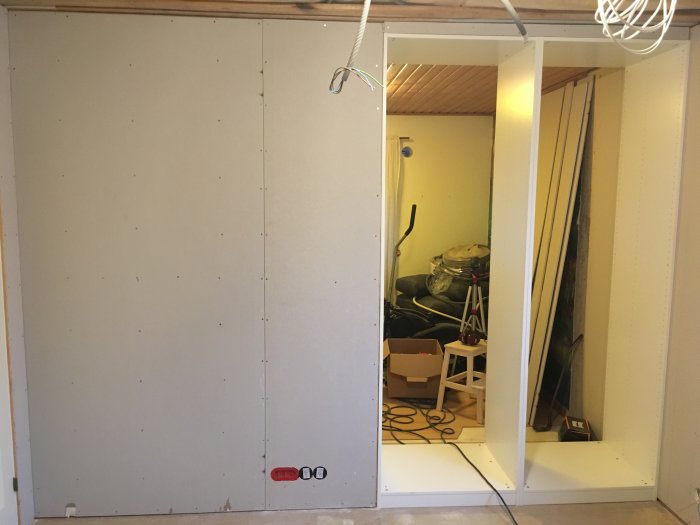 Renoverat rum med nya gipsskivor på väggen och utrymme måttat för vindstrappa, med verktyg i bakgrunden.