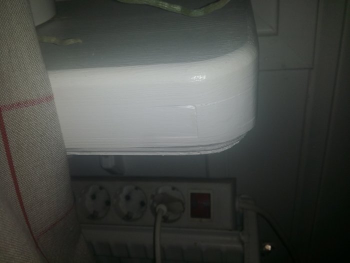 Vitmålad fönsterbänk med synliga målningslager ovanför vägguttag, nära en gardin.