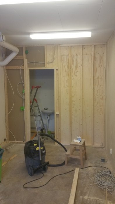 Renoveringsarbete med nytillverkade väggar av K-plywood och synlig elektrisk installation samt dammsugare på betonggolv.