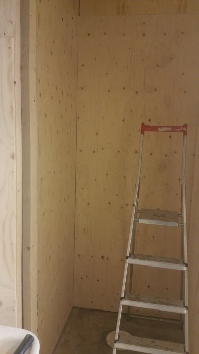 Nyvägg beklädd med K-plywood i renoveringsprojekt med stege och obehört betonggolv.