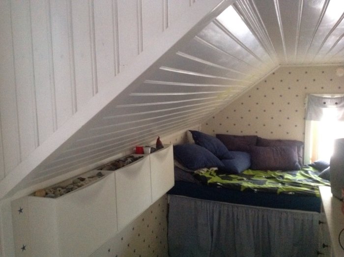 Platsbyggd säng i isolerad kattvind, utrymme under sängen dolt, vit panel och tapet med stjärnor.