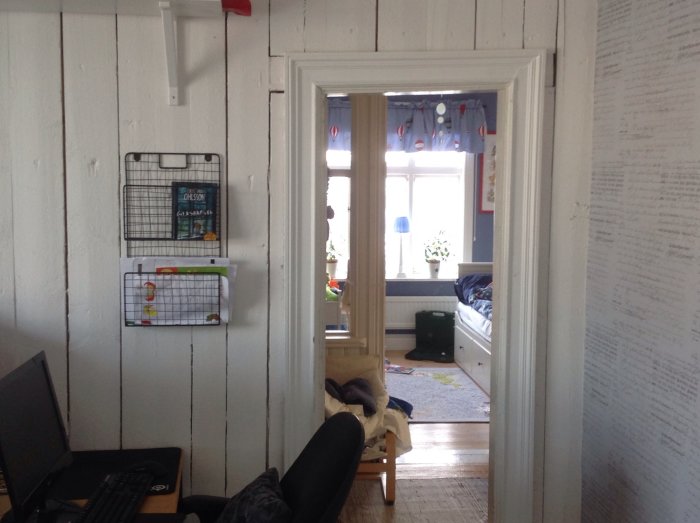 Utsikt genom öppen dörr till ett lekrum med vita plankväggar och inredning som visar användning.