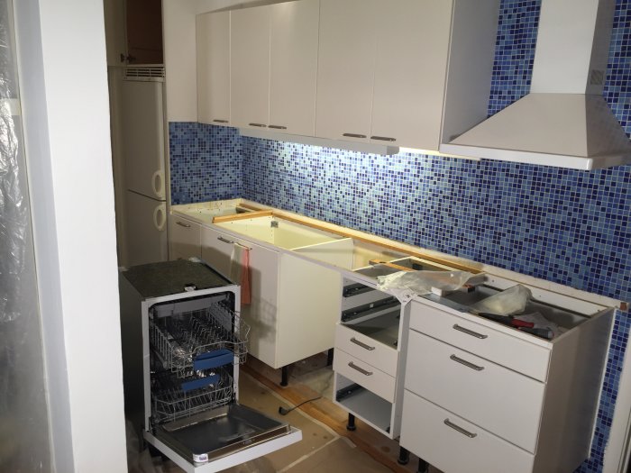 Kök under renovering med diskmaskin framme och skåpstommar utan frontpaneler.
