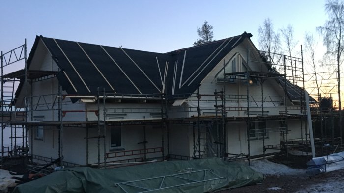 Ett hus under konstruktion med nyinstallerad takpapp och byggnadsställningar runtomkring.