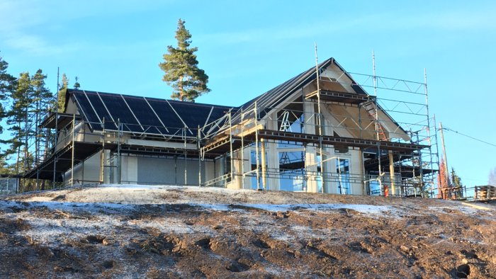 Hus under konstruktion med takpapp monterat och byggnadsställningar runtomkring.