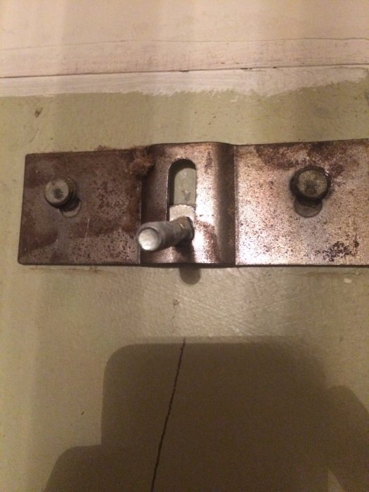Rostigt metallfäste på vägg med två rundhuvade skruvar fästa i betong.
