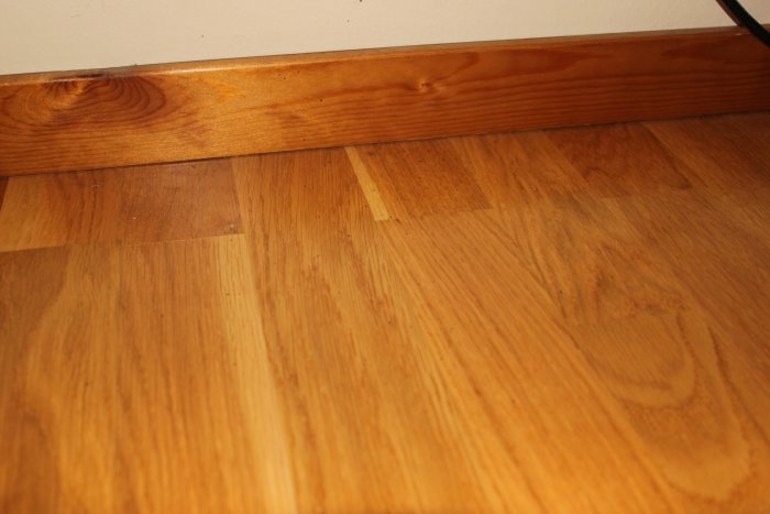 Trägolv med misstänkt svartmögel i skarven mellan golv och list i ett studentrum.