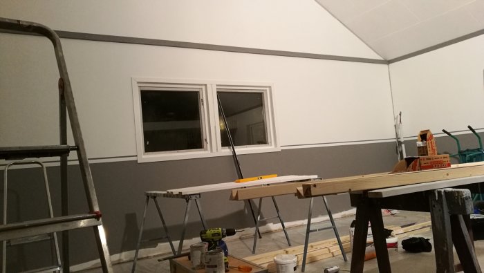 Renoverat rum med nyinstallerade vita tak- och vägglister, en stege och arbetsmaterial framför ett fönster.