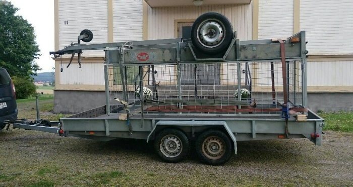 Tvåaxlad släpvagn parkerad utomhus med reservhjul och lastgaller.