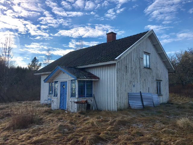 Förslagen gammal trävilla från 1909 i behov av renovering, omgiven av en stor gräsbevuxen tomt.