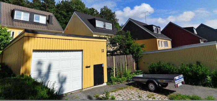 Gult hus med tillhörande garage och en parkeringsplats med släpvagn vid sidan.