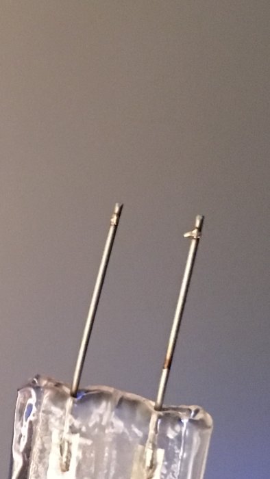 Närbild på stiftlampa med två metallstift, jämfört med mindre G4-lampa.