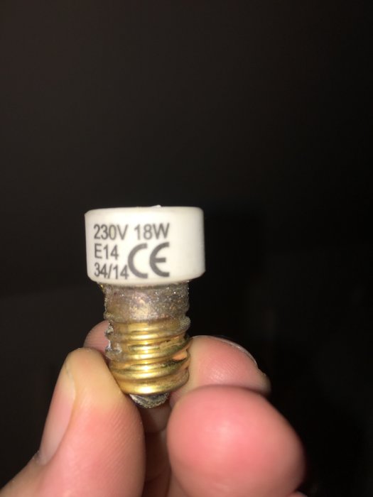 En hand håller en gängad E14-lampsockel med tydlig märkning 230V 18W.
