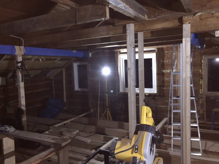 Kattvind under renovering med nya limträbalkar, verktyg och upplyst av arbetslampa.
