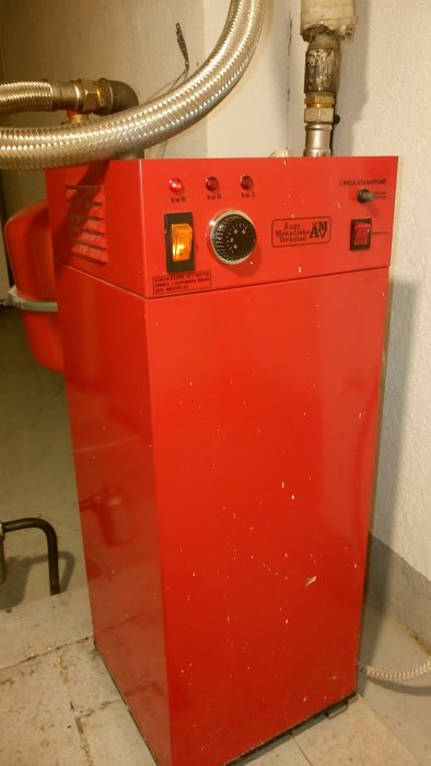 Äldre röd elpanna med inställningskontroller och indikatorlampor för 6kW och 3kW i ett pannrum.