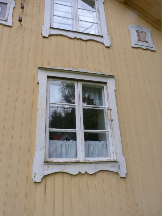 Gul fasad på landet med fönster behövande ommålning.