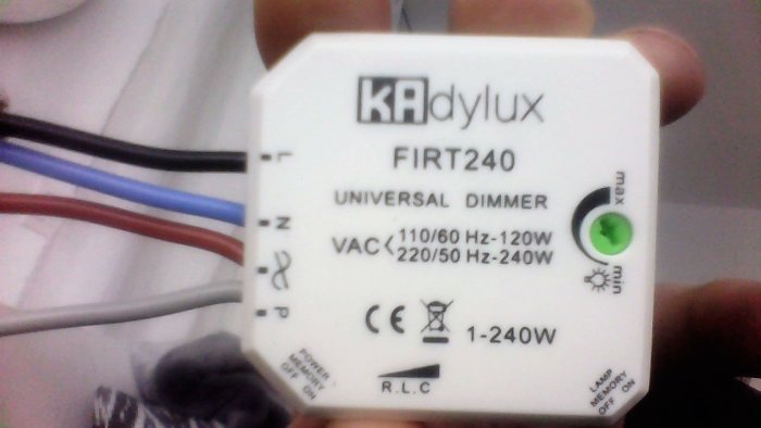 Hand som håller en vit KAdylux universal dimmer med elektriska anslutningar och teknisk specifikation synlig.