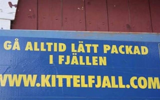 Blå skylt text "Gå alltid lätt packad i fjällen", webbadress "Kittelfjäll", rödbrun bakgrund.