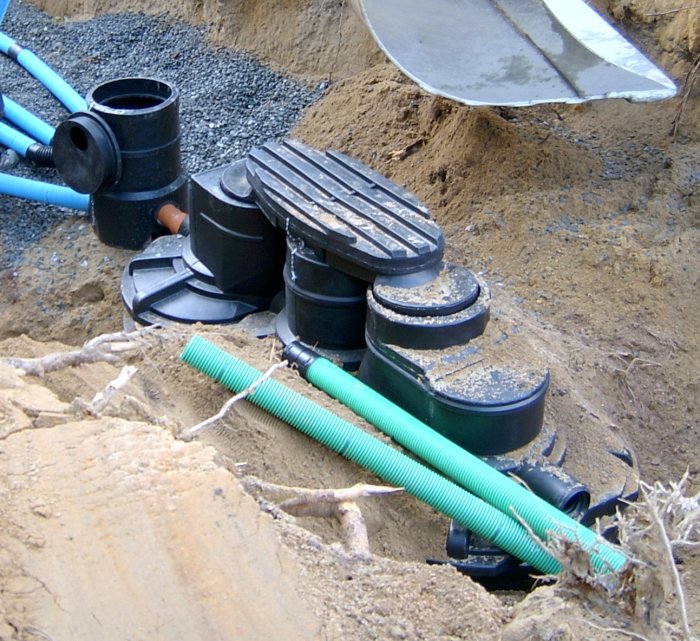 Slamavskiljare från 2007 i en grävd grop med röranslutningar och en spade i bakgrunden.