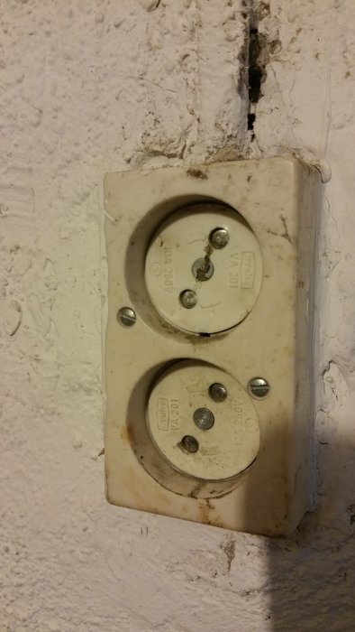 Gamla, smutsiga och ojordade dubbla vägguttag i en källare.