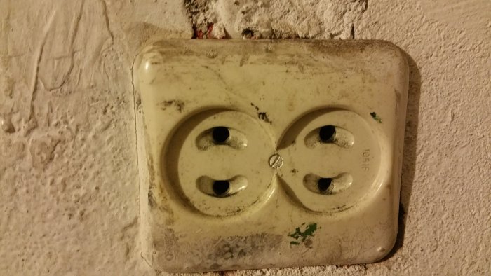 Ett smutsigt och ojordat dubbeluttag i en sliten tillstånd monterat på en vägg.