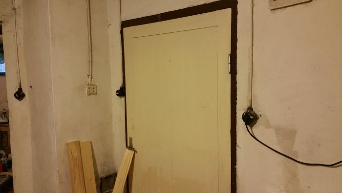 Ett ojordat vägguttag i en sliten källare, omgivet av två svarta strömbrytare och elledningar.