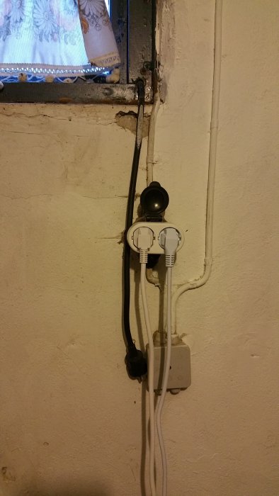 Eluttag och strömbrytare på en vägg med synlig kabeldragning och en grenuttag utan jordanslutning.