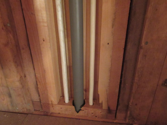 Vertikala träramar som griper i varandra och en synlig rörinstallation mot en trävägg.