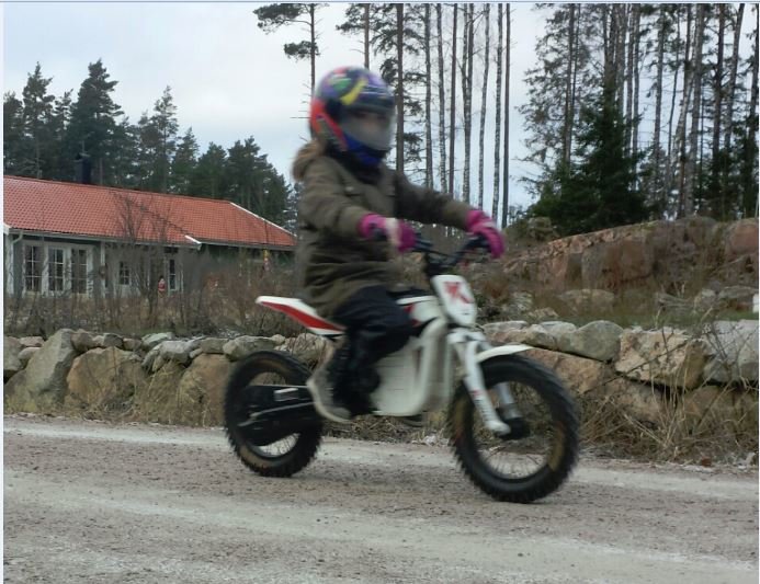 Barn i vinterkläder kör en liten motorcykel på en grusväg nära skogen.