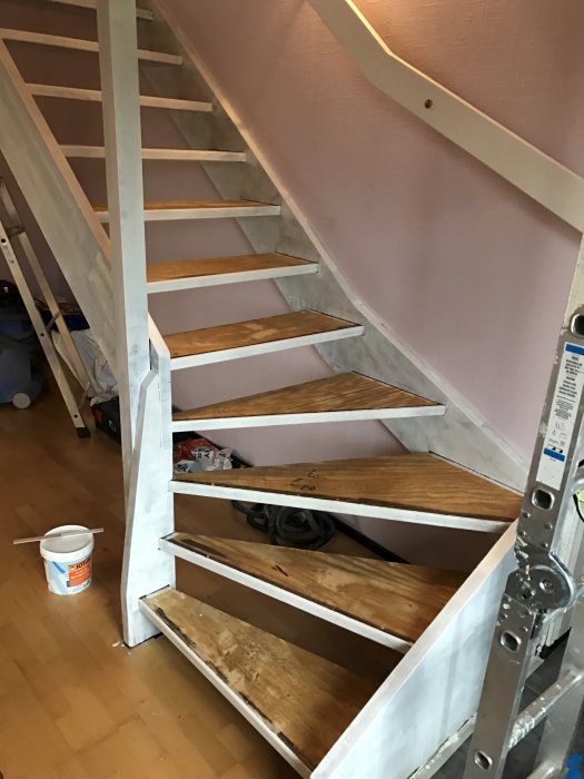 Trappa under renovering med grundfärg applicerad, ommålade vita sidor och trästeg.