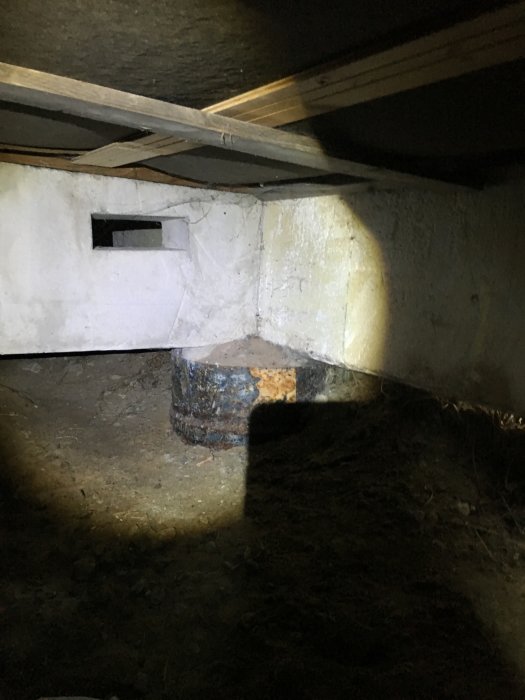Mörk och smutsig krypgrund med ojämnt gjutna plintar, slarviga stöd och synlig påväxt, indikerar potentiella underhållsproblem.