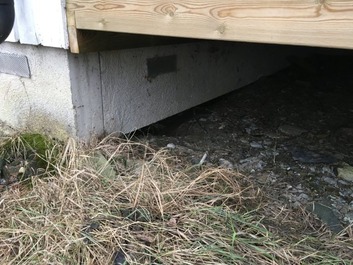 Krypgrund under hus med synliga konstruktionsbrister, slarvigt gjutna plintar och skräp.